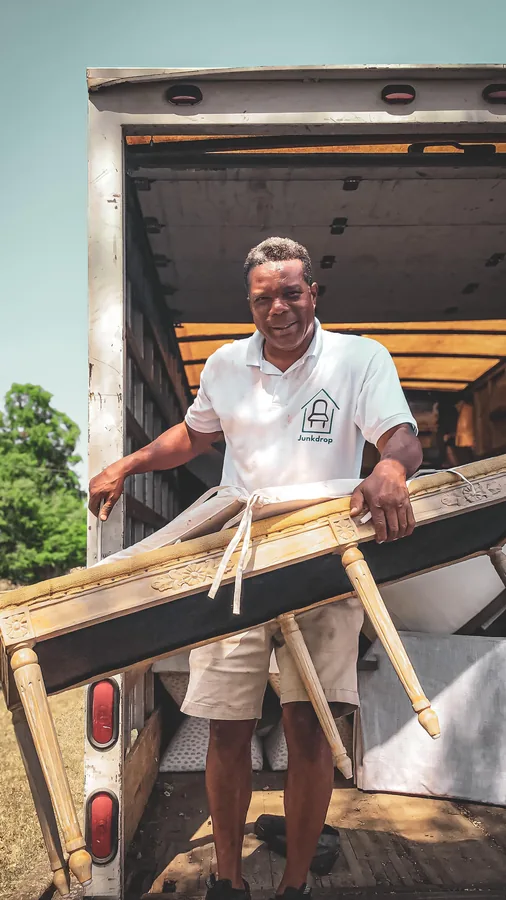 Junkdrop crew member carrying wooden furniture beside a truck