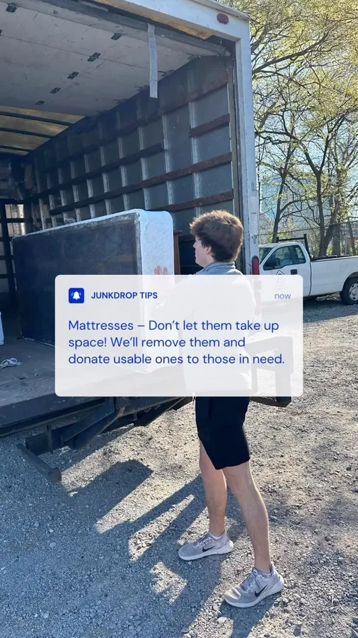 Crew member carrying a mattress beside a Junkdrop truck